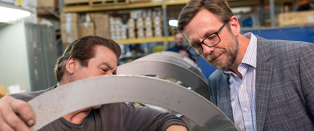 Welder and business owner inspecting large scale specialized machinery.