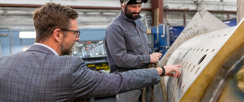 business owner and welder inspecting large specialized machinery.