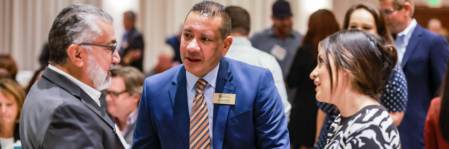 Three business people and professionals engaged in conversation at a networking event. 